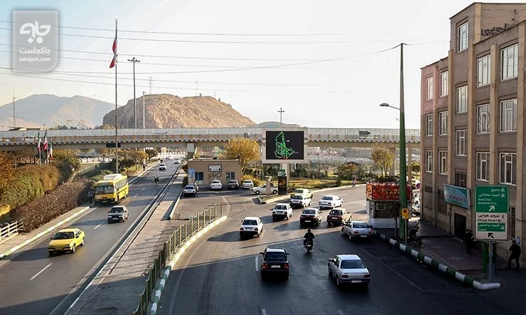 خیابان پیروزی تهران با خودروها و اتوبوس زرد، پل بزرگراه و تپه دوشان‌تپه در پس‌زمینه