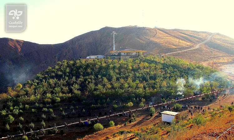 دامنه سرخ‌رنگ کوه عینالی تبریز با ردیف درختان کاشته‌شده و مسیرهای پیاده‌روی در نور آفتاب آبان